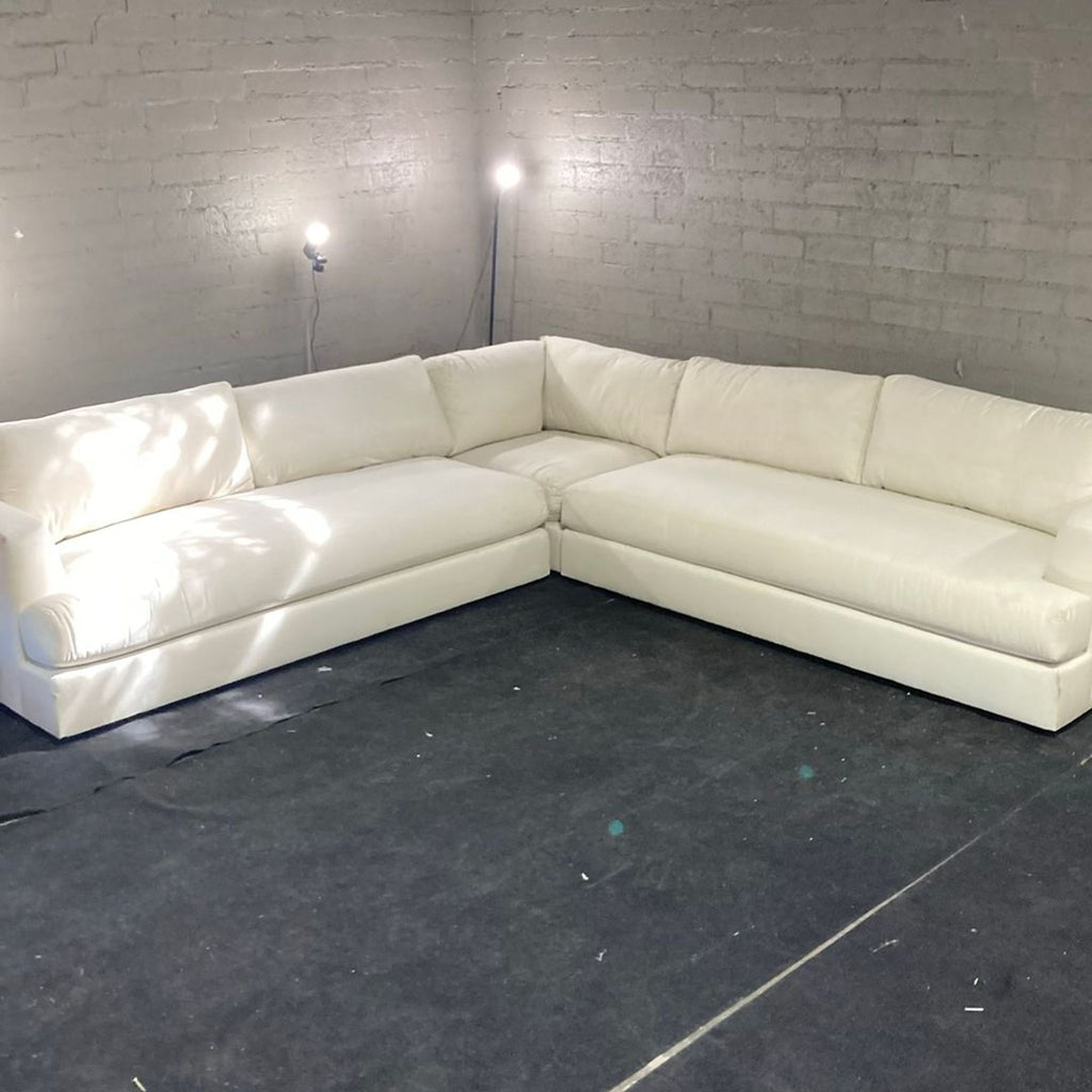 1. White Maiden Home sectional sofa in a corner, with plush seating and brick walls illuminated by floor lights.  