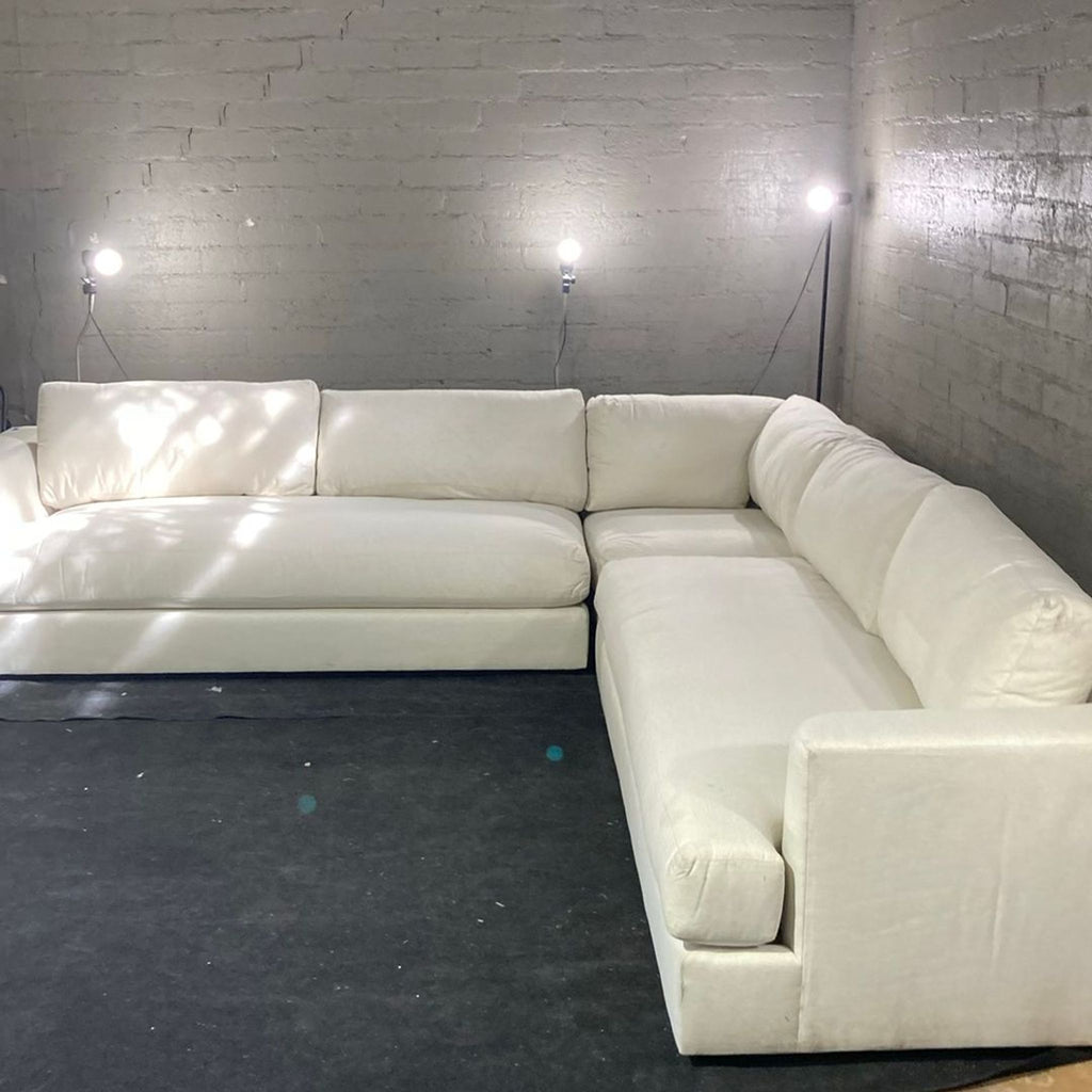 3. Angled shot of a Maiden Home sectional sofa, upholstered in white, set against gray brick walls with floor lamps.