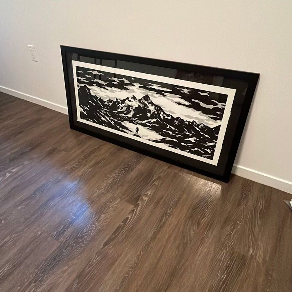 Dramatic monochrome landscape art print shows mountains and a solitary figure, framed and ready to hang.