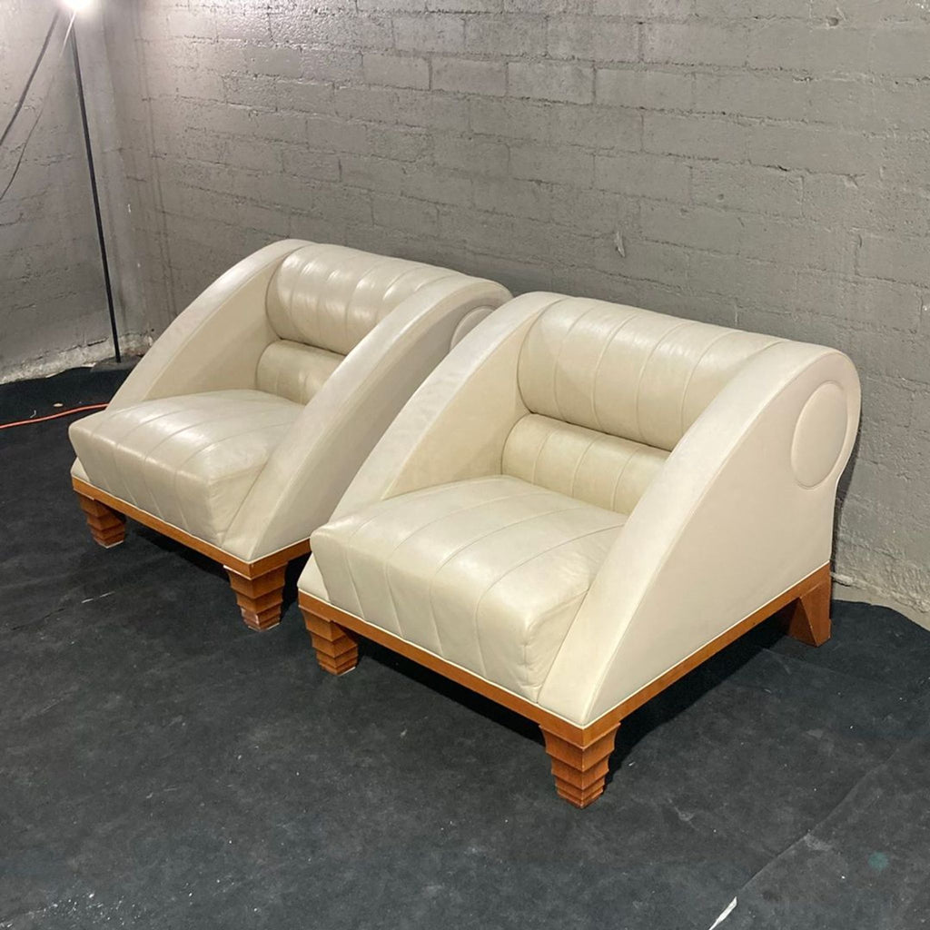 Two cream leather Giorgetti club chairs with curved arms and sturdy wood bases, perfect for stylish lounging.