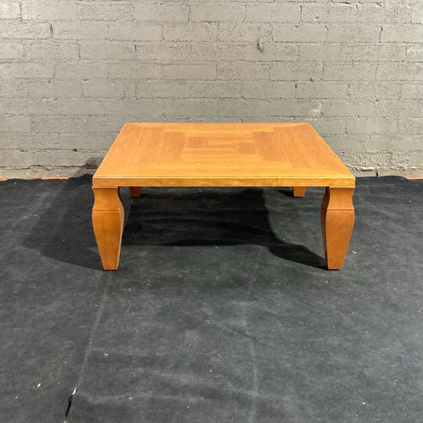 1. Giorgetti coffee table with a square wooden top and solid curved legs, set against a gray brick wall.
