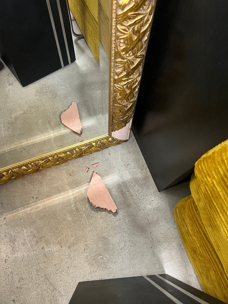 1. Ornate gold-framed mirror with broken decorative corner, missing piece and fragments on concrete floor.
