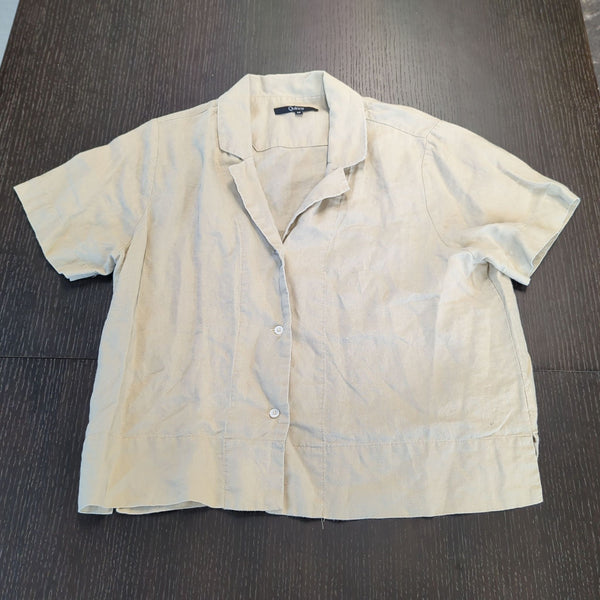 1. Light beige short-sleeve button-up women's shirt from Quince shown laid flat on a dark surface.  