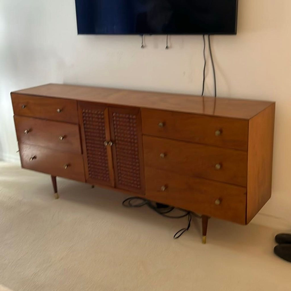 Wood-finished entertainment center featuring six drawers, a detailed central cabinet, and brass-accented sturdy legs.