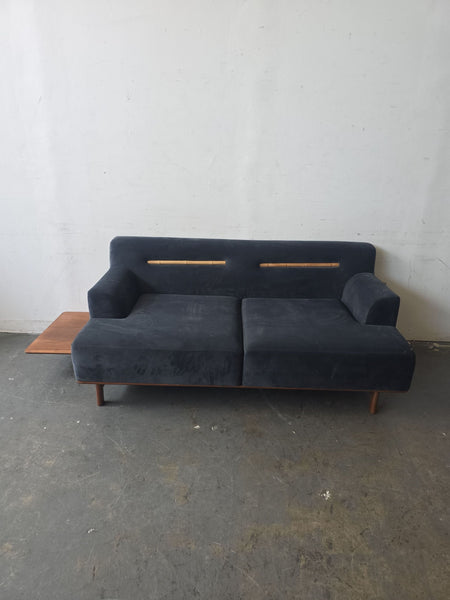 Deep blue sectional with wooden legs, a backrest accent, and a built-in side table for added functionality.