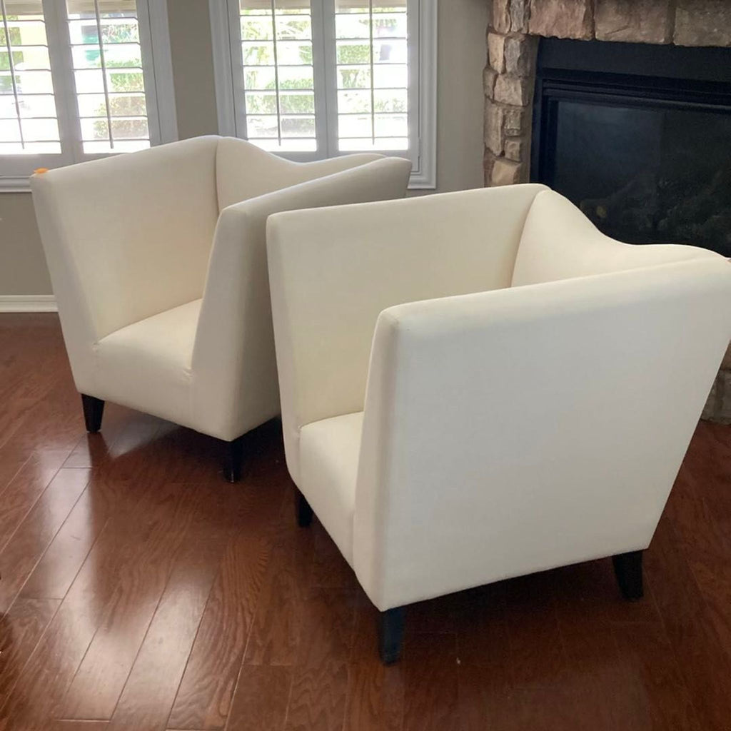 Pair of modern cream lounge chairs by Shabby Chic, featuring sleek lines and sturdy wooden legs for stylish comfort.