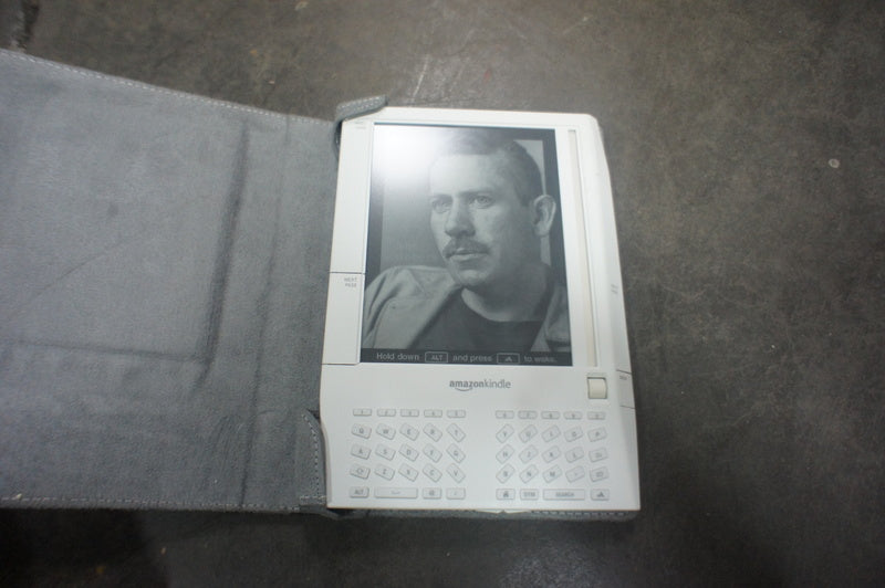 1. Amazon Kindle e-reader with a keyboard, open gray cover, showing a grayscale display on a gray surface.