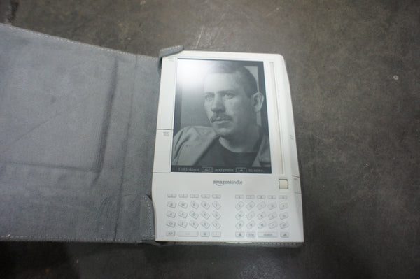 1. Amazon Kindle e-reader with a keyboard, open gray cover, showing a grayscale display on a gray surface.