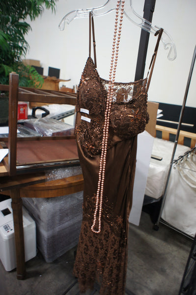 1. Brown lace Bicici women's dress with floral details and a long pearl necklace draped on hanger.