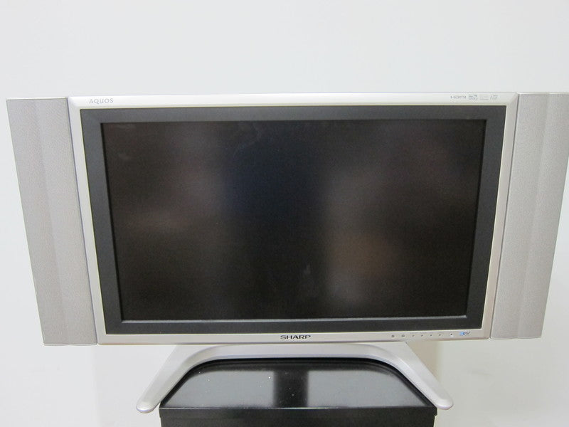 1. Front view of a Sharp Aquos LC-26GD4U LCD TV with integrated side speakers on a silver stand.  