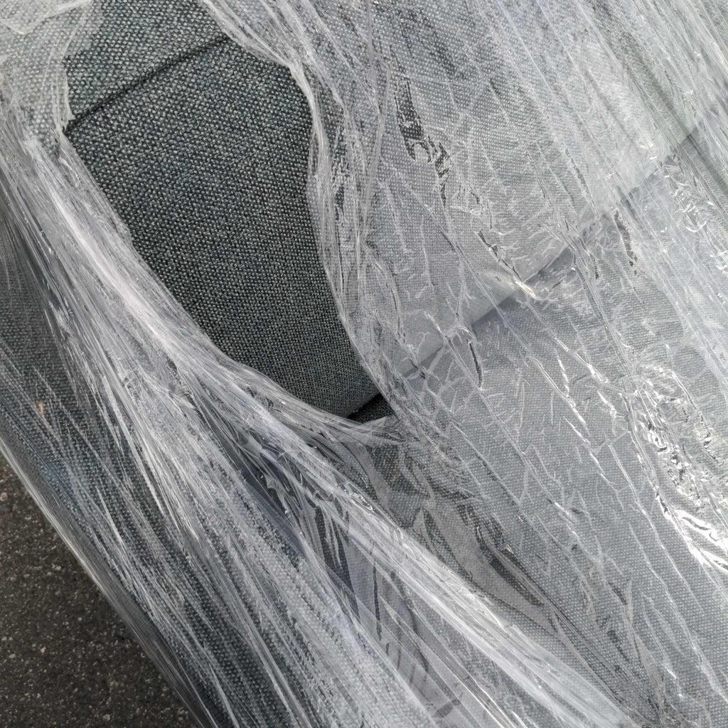 Gray fabric 3-seat sofa partially wrapped in clear protective plastic covering.