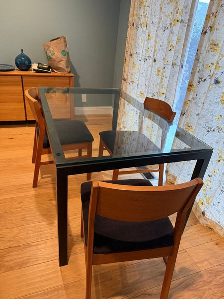 1. Crate and Barrel glass-top dining table with black frame, paired with wood chairs and floral curtains.  