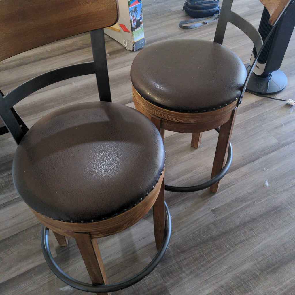 1. Two brown round bar stools with padded seats, wooden legs, and black metal footrests on a wood floor.
