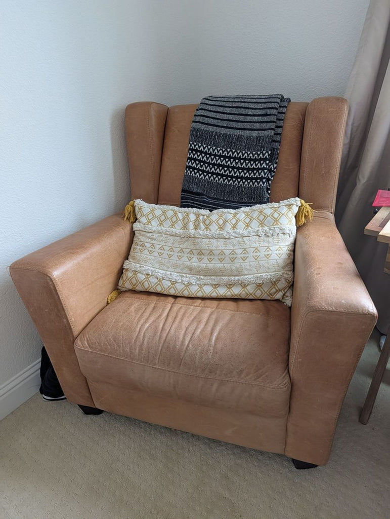 1. Westelm tan leather lounge chair with a patterned pillow and blanket, placed in a corner next to a table.