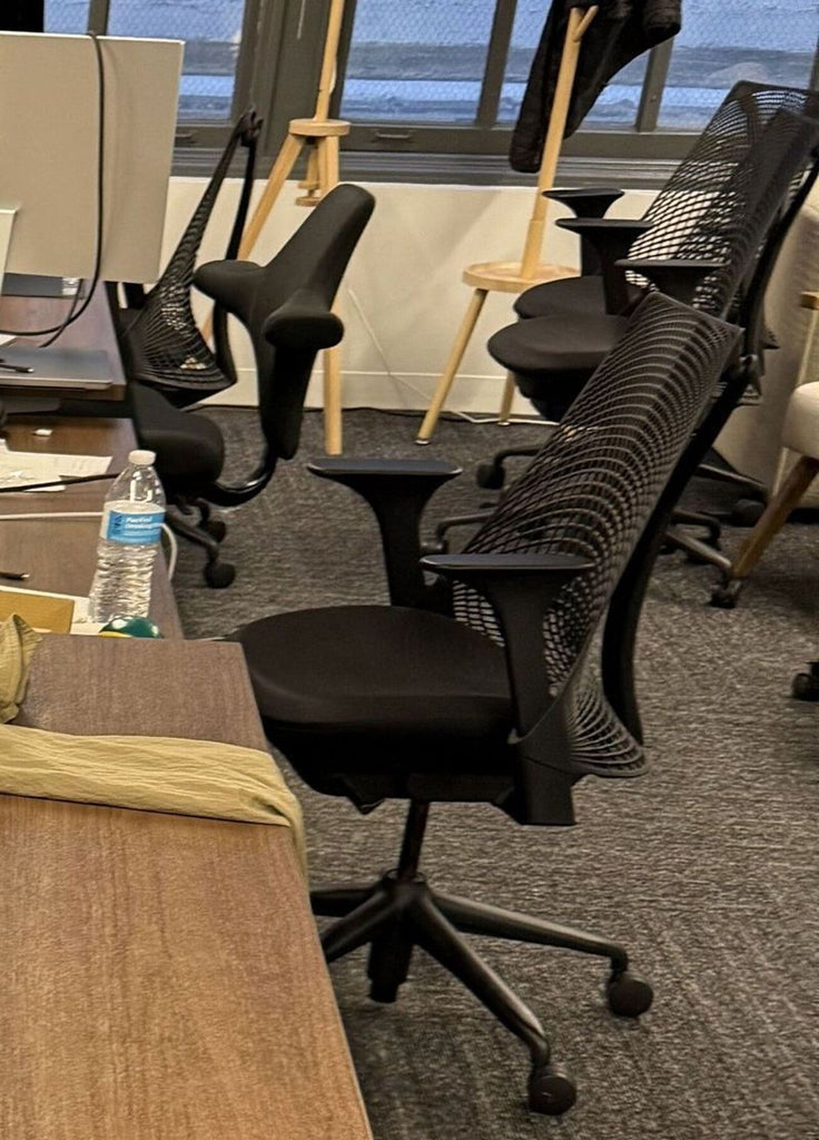 1. Black Herman Miller office chair with mesh backrest and wheels, located in a modern workspace near desks.