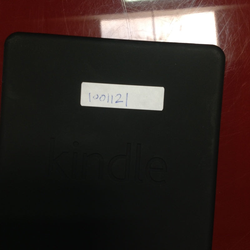 2. Back view of a black Amazon Kindle with a white label and engraved logo, on a red table.