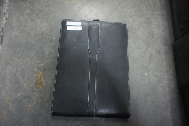 3. Full view of closed black Amazon Kindle case with white labels on top left, placed on gray floor.
