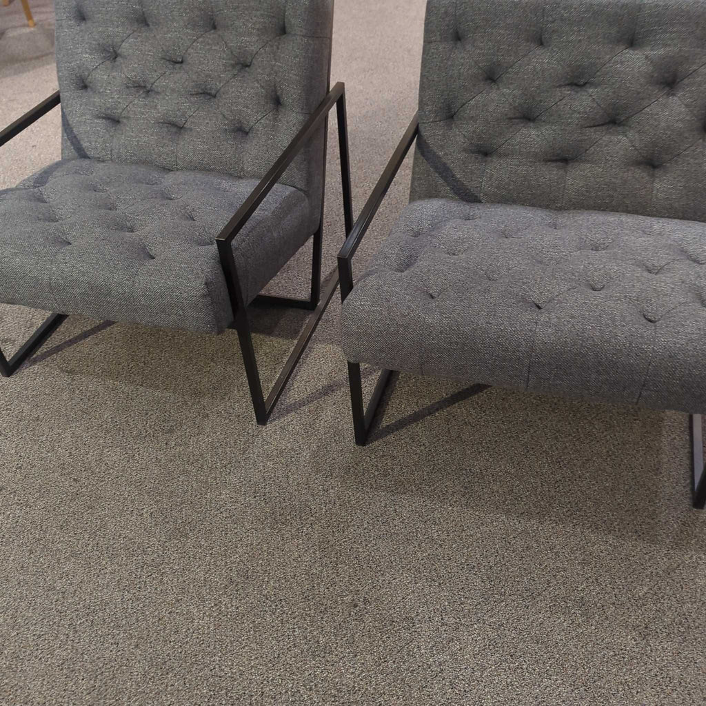 1. Two Alder & Tweed lounge chairs with tufted grey upholstery and black metal frames on a carpeted floor.