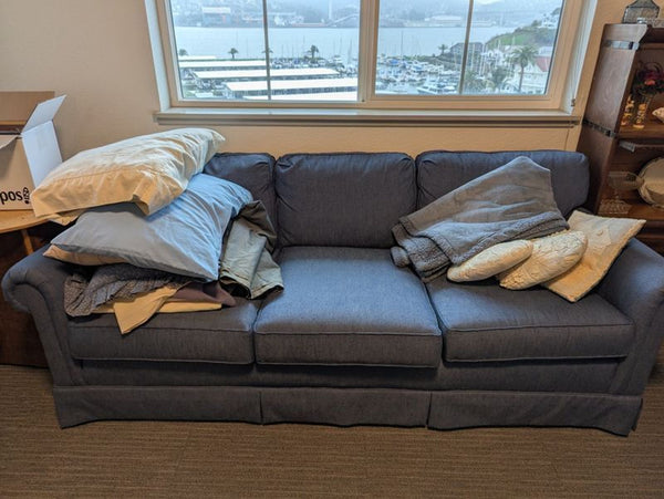 1. Blue Reperch 3-seat sofa with scattered bedding and pillows near a window in a lived-in room.  