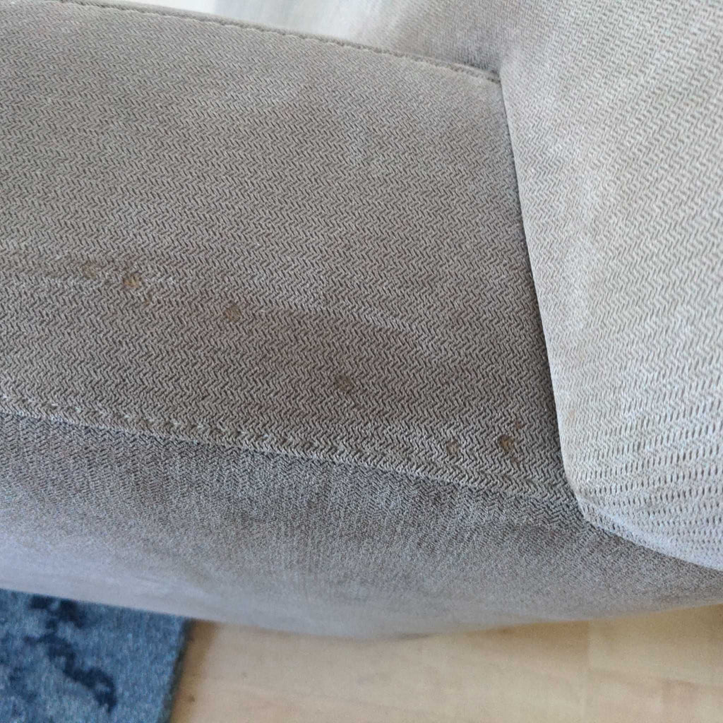 2. Close-up of the armrest and cushion of a taupe Crate and Barrel 3-seat couch showing minor stains.