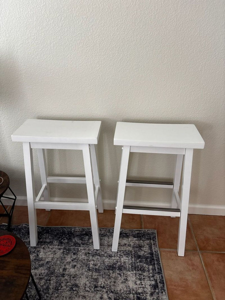 1. Two white wooden bar stools with rectangular seats and footrests placed side by side against a wall.