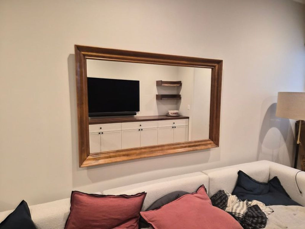 Large rectangular mirror with a simple, modern frame, reflecting light from a nearby window.