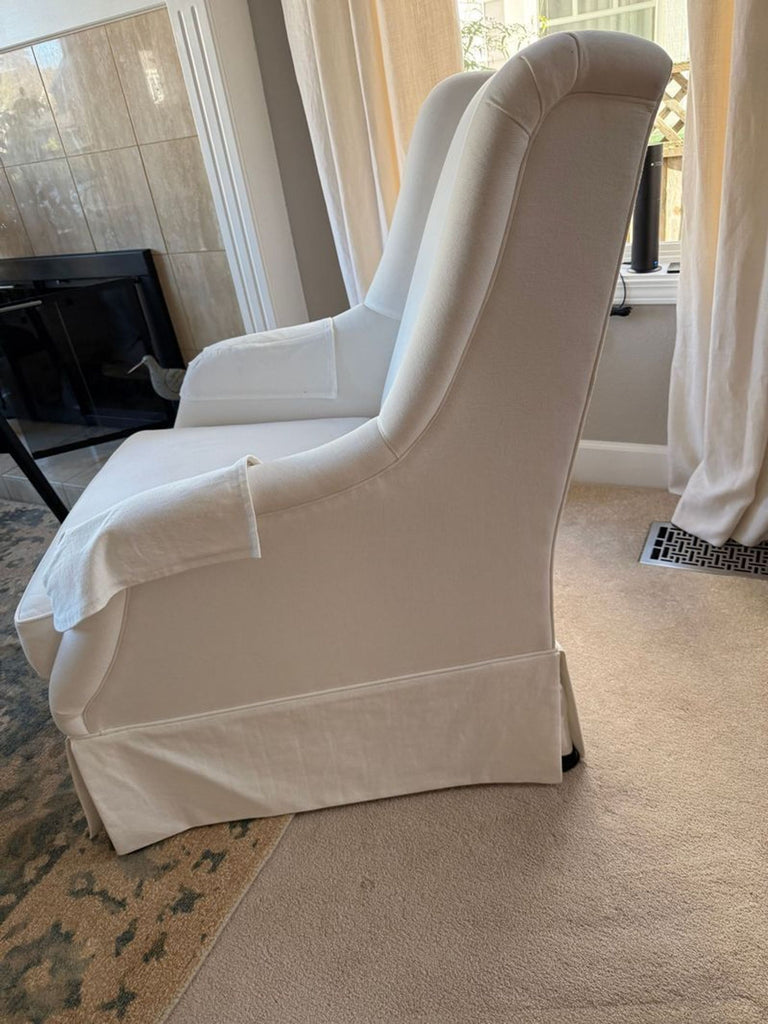 2. Side view of a Reperch white lounge chair with skirted base and armrest covers, set on neutral carpeting.  