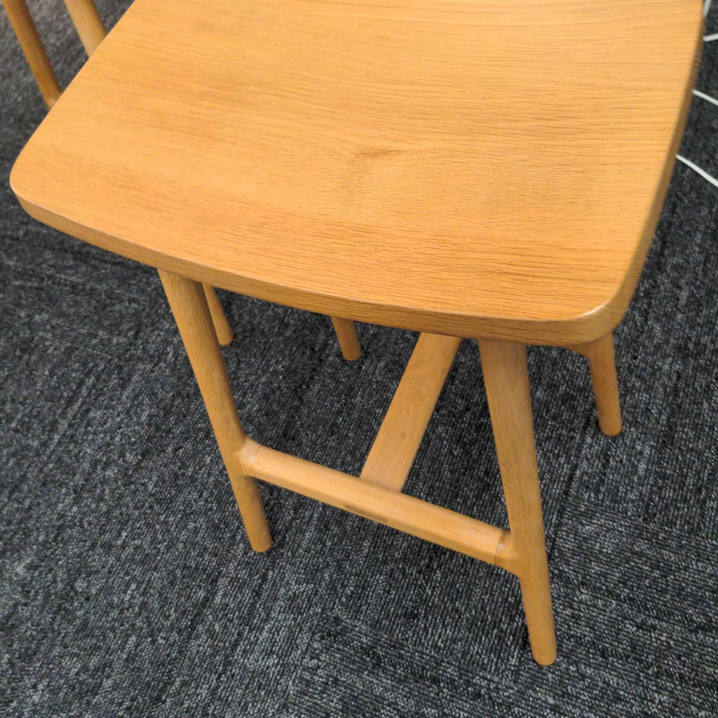 2. Close-up of a single Article wooden stool, highlighting its smooth curved seat and angled legs.