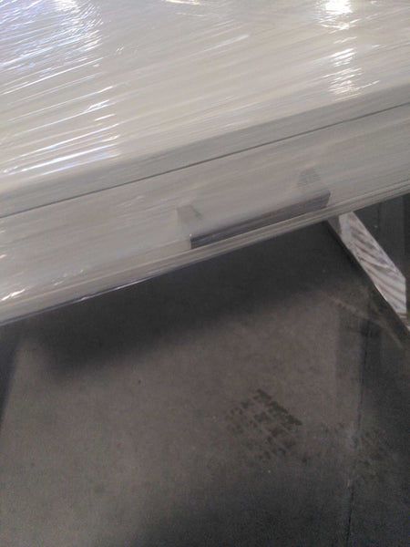 1. Close-up of a modern desk drawer wrapped in protective plastic with a metal handle visible.