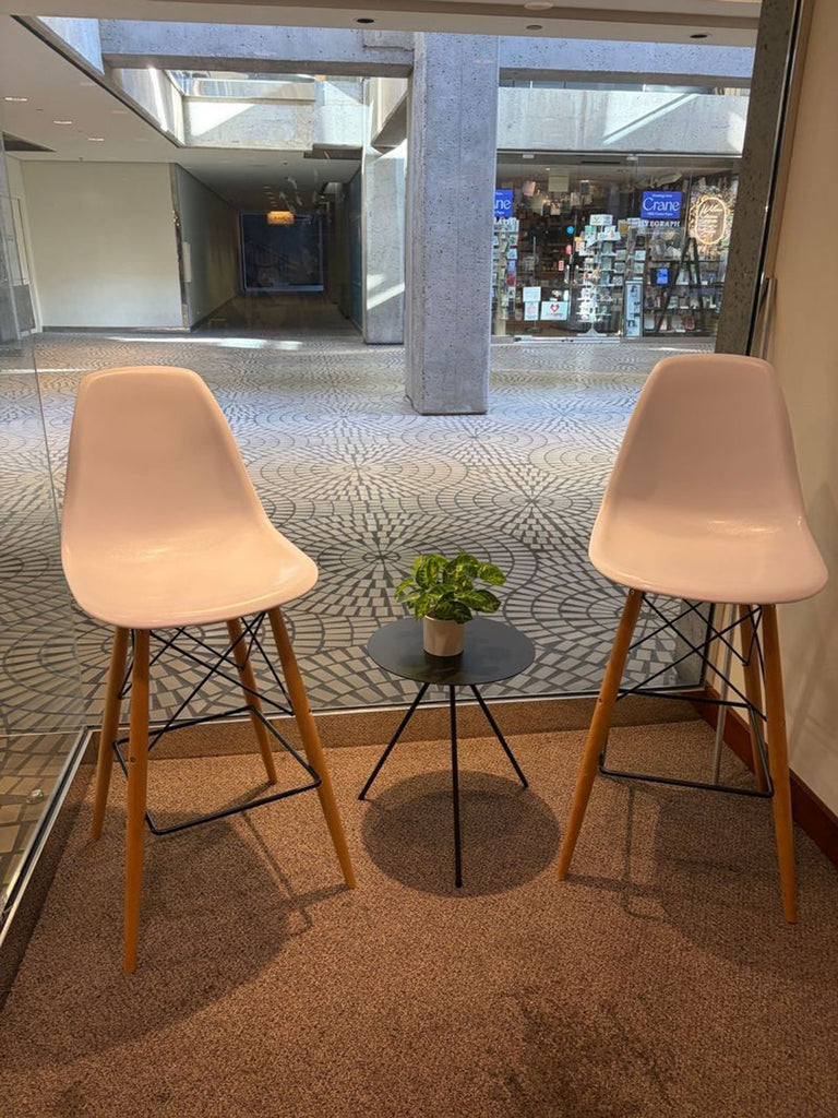 - Two modern dining chairs with white seats and wooden legs, placed beside a small black round table.