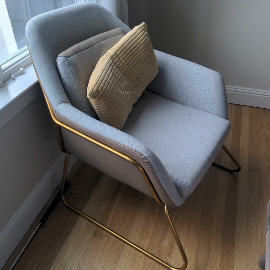 1. Modern Reperch lounge chair with light grey upholstery, gold frame, and two beige cushions by a window.