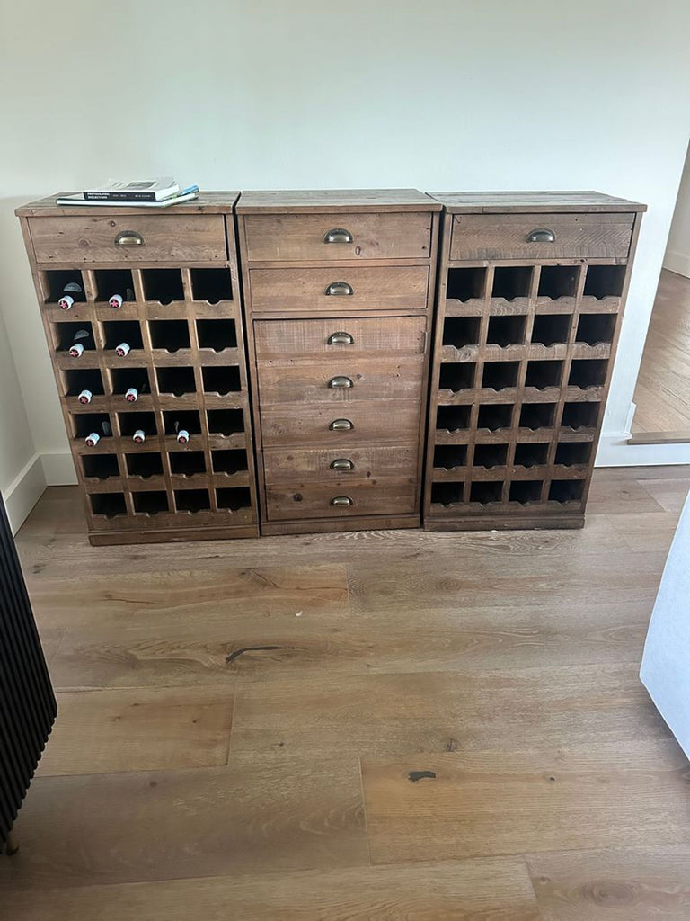 1. Pottery Barn wooden wine storage cabinet set with drawers, cubby holes, and books on top, against a white wall.