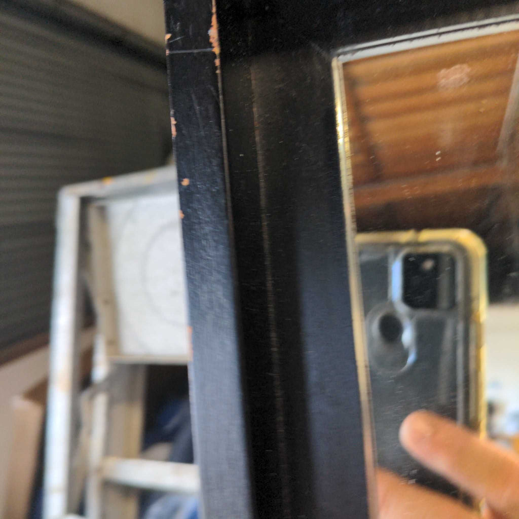 2. Close-up of the West Elm mirror's black frame showing minor scuffs and chipped paint on the edge.