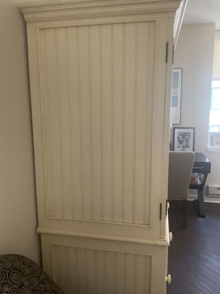 1. Cream-colored wooden armoire with paneled doors in a corner, next to patterned furniture and soft lighting.