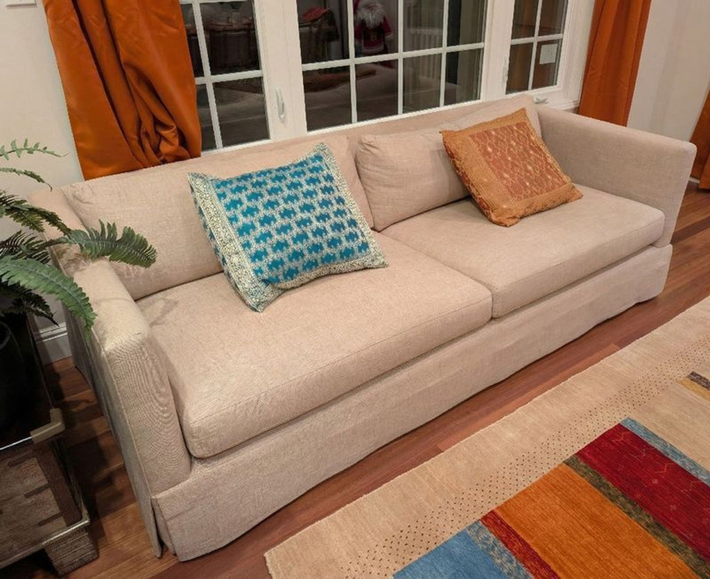 2. Contemporary Crate and Barrel loveseat in cream fabric, styled with orange and blue accent pillows in a bright space.