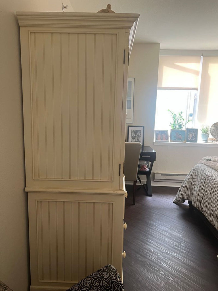 2. Tall cream-colored hutch and armoire with vertical grooves, placed in a bright, modern bedroom near a window.