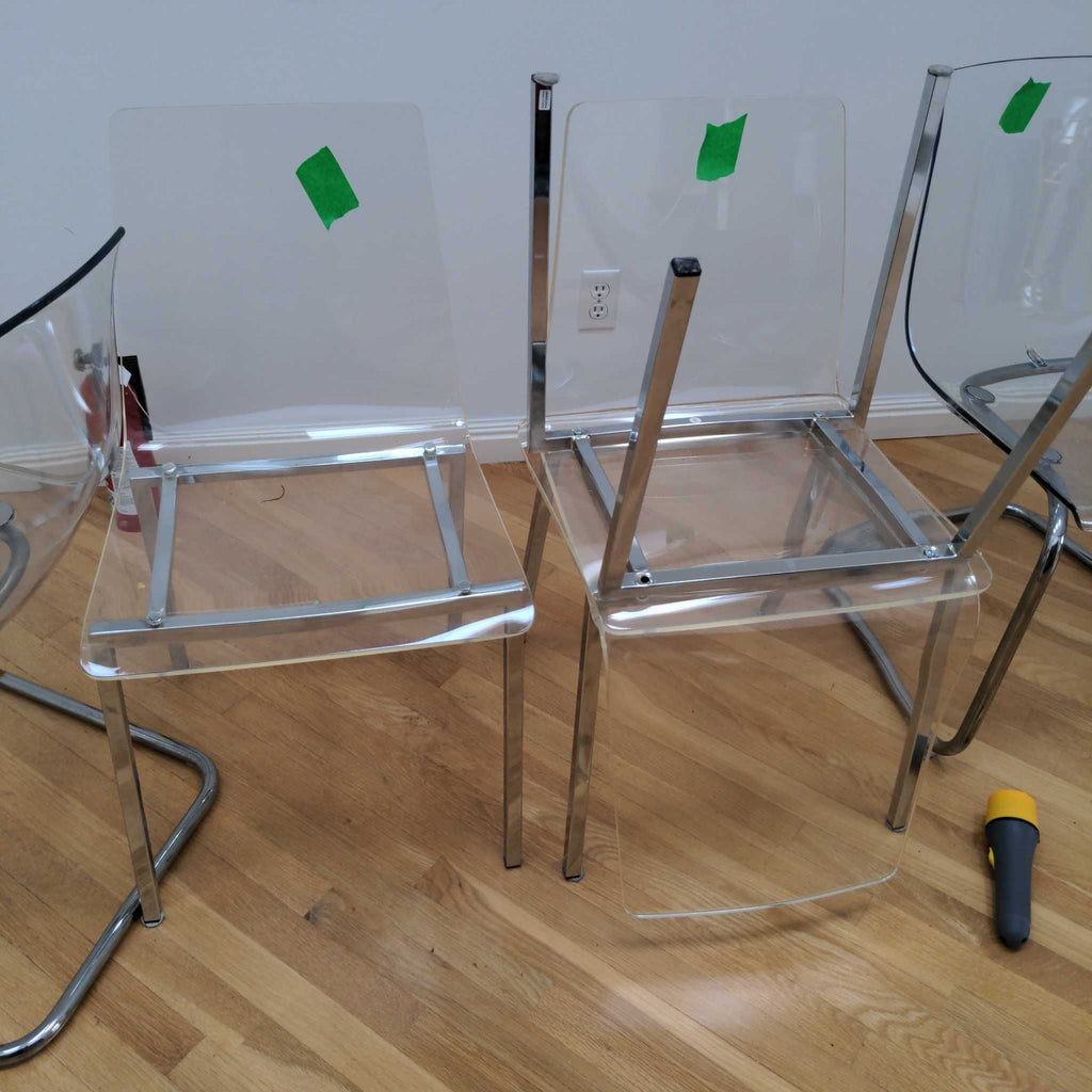 1. Set of modern clear acrylic dining chairs with chrome frames, some partially assembled, on a wooden floor.