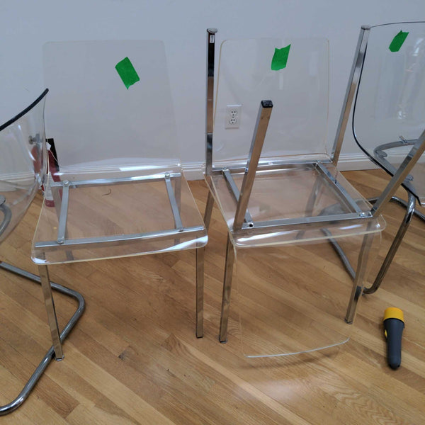 1. Set of modern clear acrylic dining chairs with chrome frames, some partially assembled, on a wooden floor.