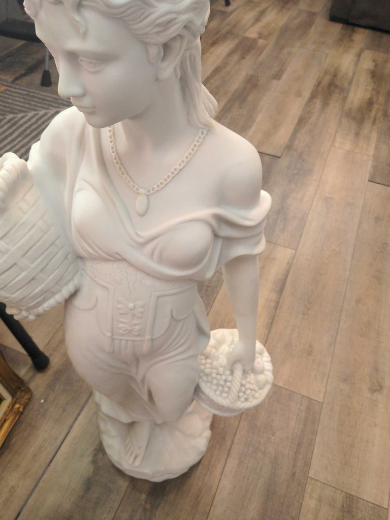 a white marble statue of a woman holding a basket of fruit.