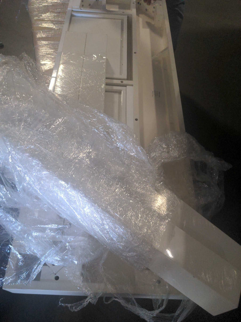 Unassembled West Elm side and console table with white parts covered in protective plastic wrap.