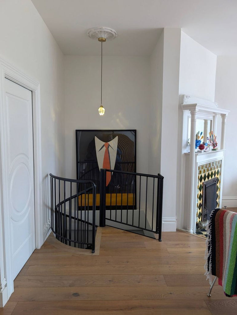 1. Framed print of a suit and orange tie hangs in a modern room near a spiral stair gate and fireplace.