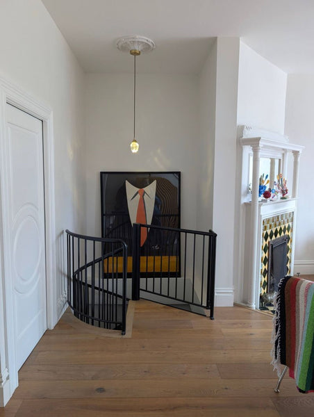 1. Framed print of a suit and orange tie hangs in a modern room near a spiral stair gate and fireplace.