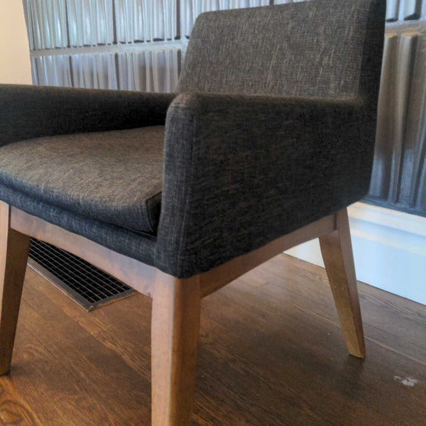 1. Dark gray upholstered dining chair with wooden legs, angled armrests, and a modern design on wood flooring.