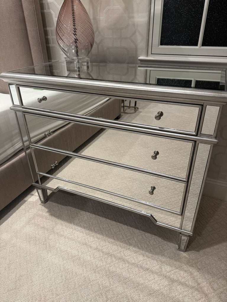 Mirrored dresser with three drawers, metallic trim, and crystal knobs, placed in a modern bedroom setting.