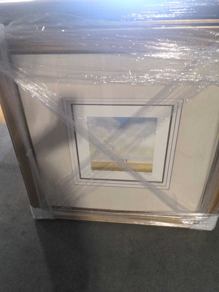 1. Framed painting of two figures walking on a beach, covered in protective plastic wrap, under soft lighting.