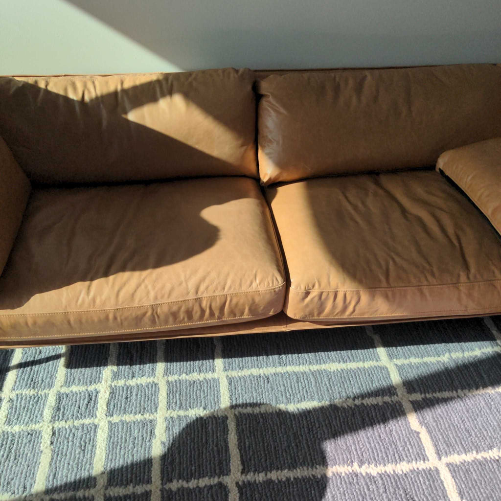 Crate & Barrel tan leather 3-seat sofa shown in sunlight on a patterned rug, highlighting soft cushions.