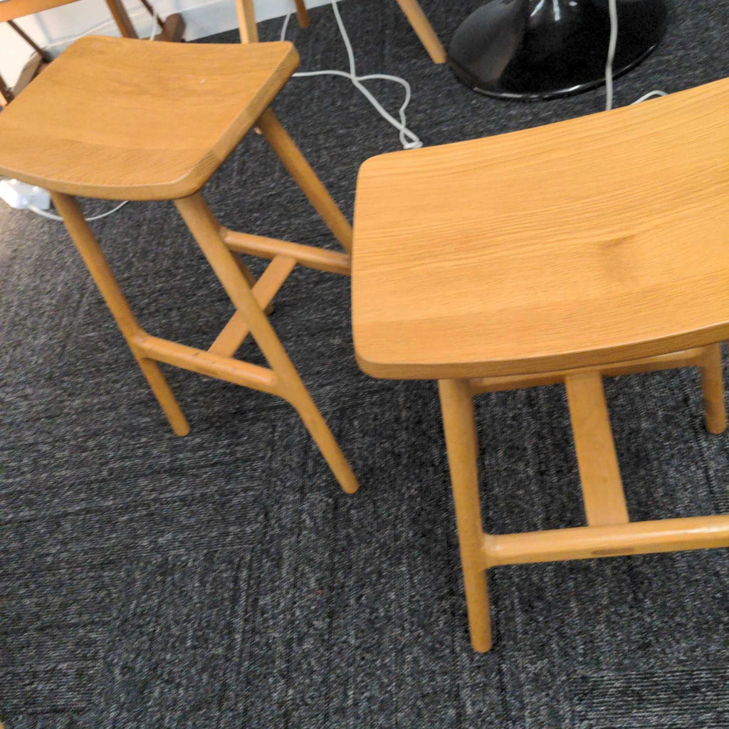1. Pair of Article brand wooden stools with curved seats and minimalist design on dark carpet flooring.