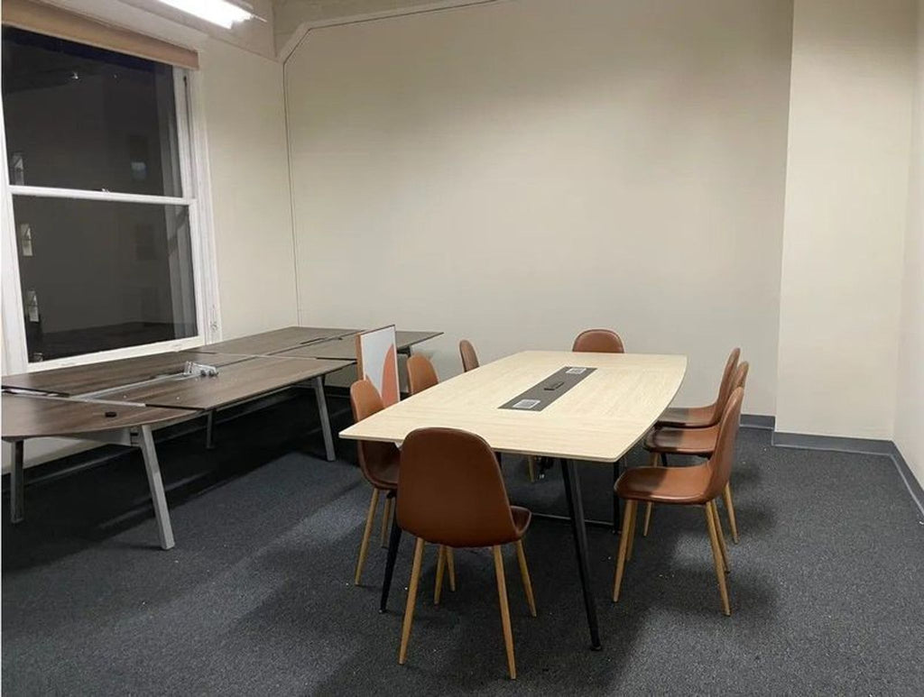 Brown dining chairs with wooden legs are arranged around a light table in a modern, carpeted room.  