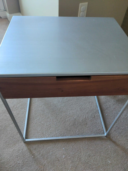 1. CB2 end table with a gray metal top, wood drawer, and minimalist metal frame on carpet flooring.