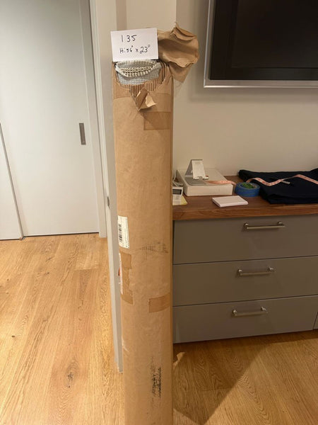 1. A large cylindrical package partially opened, revealing a roll of fabric and a label reading "135 H: 56" x 23”.  